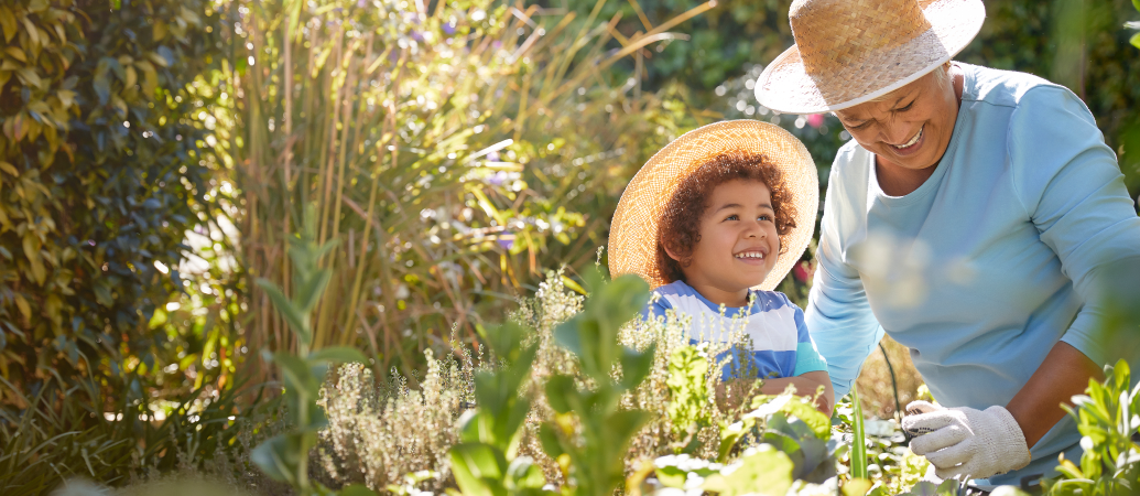 Older woman working in garden with smiling young child.